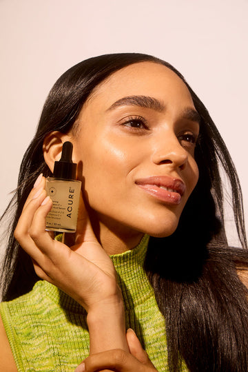 Woman holding Acire Serum next to her face focusing on bright, smooth skin